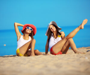 Two women enjoying a sunny day, sitting together on the beach with waves gently lapping at the shore.